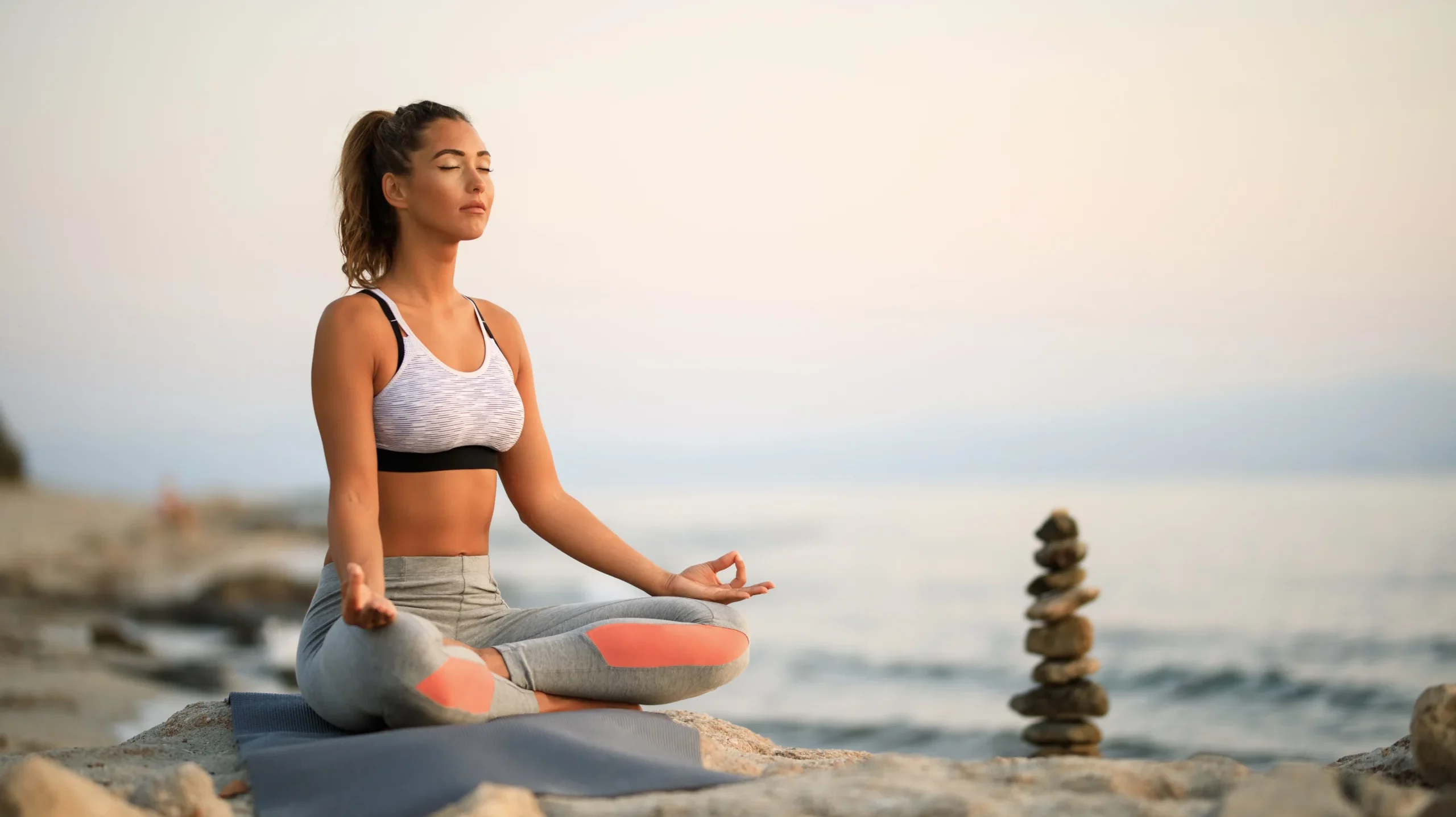 young-woman-practicing-yoga-relaxation-exercises-meditating-rock-beach